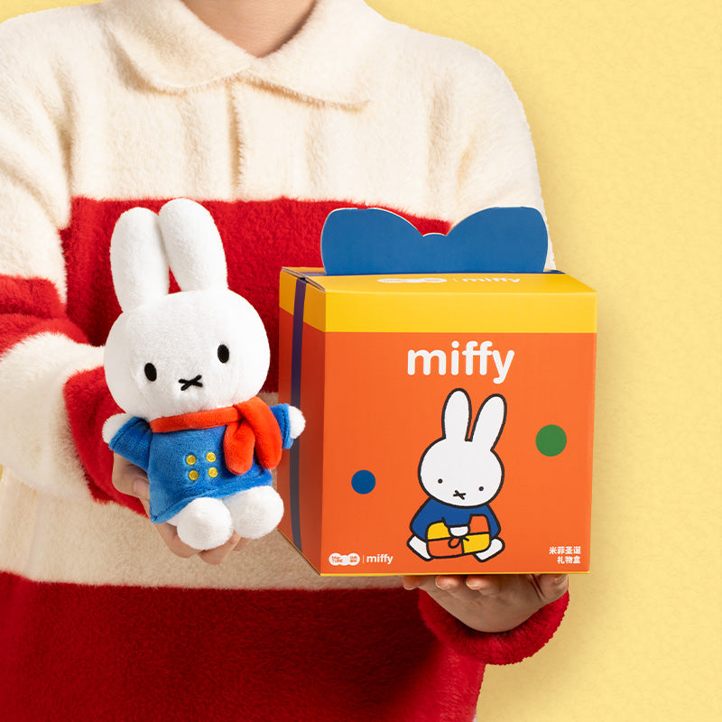 Miffy plush toy in blue coat and orange scarf held alongside its matching branded gift box