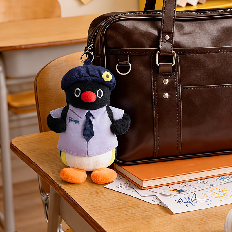 Pingu plush keychain attached to a brown leather school backpack